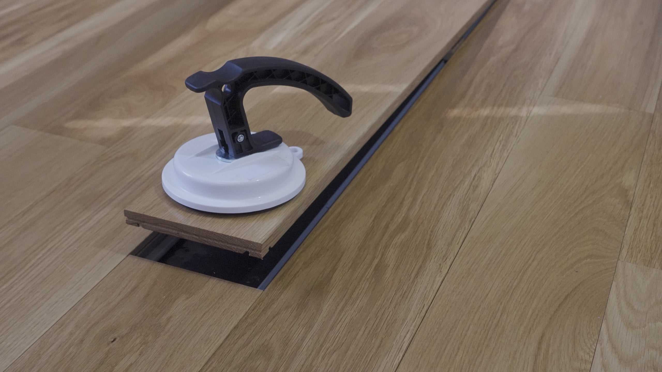 Installation process of solid wood floors on concrete slab using Steller Floors assembly system, featuring a suction cup tool for easy plank removal.
